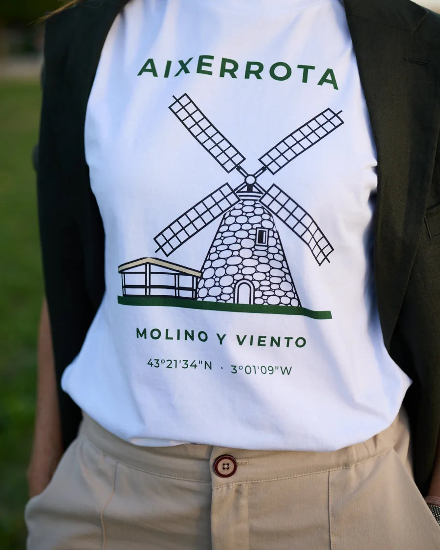Detalle de la camiseta blanca Aixerrota · Molino y Viento bajo una chaqueta verde oscuro, con el molino, el lema y las coordenadas