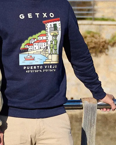 Detalle de la sudadera Getxo · Puerto Viejo con el dibujo y las coordenadas, con la mano en la barandilla
