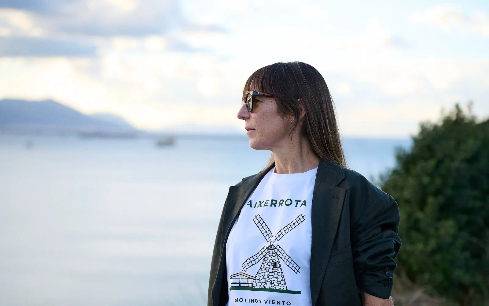 Una mujer con la camiseta Aixerrota, de pie junto a la ría de Getxo, mirando al horizonte en una tarde de octubre