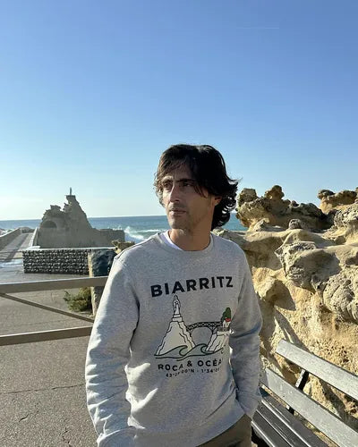 Hombre con la sudadera gris Biarritz · Roca & Océano, caminando por el paseo junto al mar