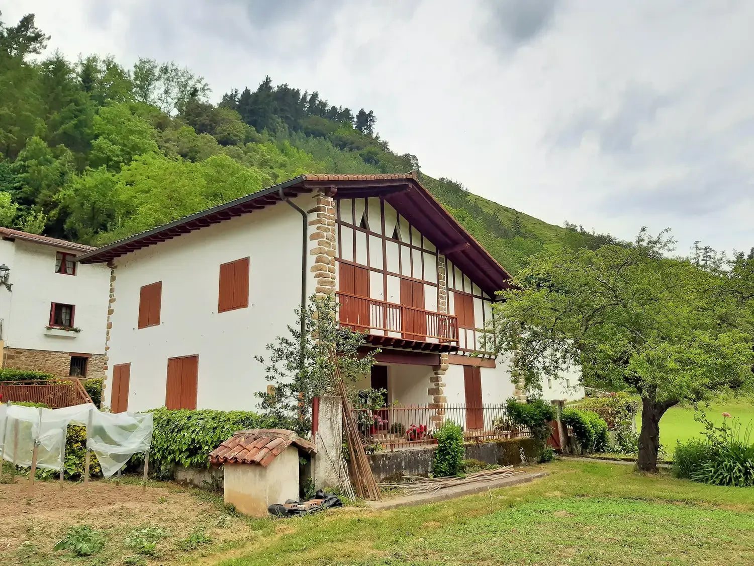 Sara etxea, caserío de Ataun (Gipuzkoa): fachada blanca con entramado de madera rojo y un árbol delante